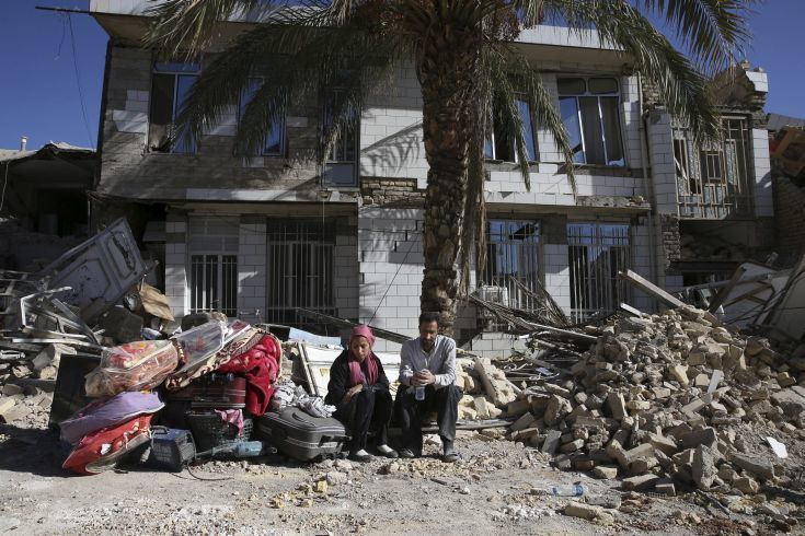 Survivors sit in front of a destroyed house on the earthquake site in Sarpol-e-Zahab in western Iran, Tuesday, Nov. 14, 2017. Rescuers are digging through the debris of buildings felled by the Sunday earthquake in the border region of Iran and Iraq. (AP Photo/Vahid Salemi)